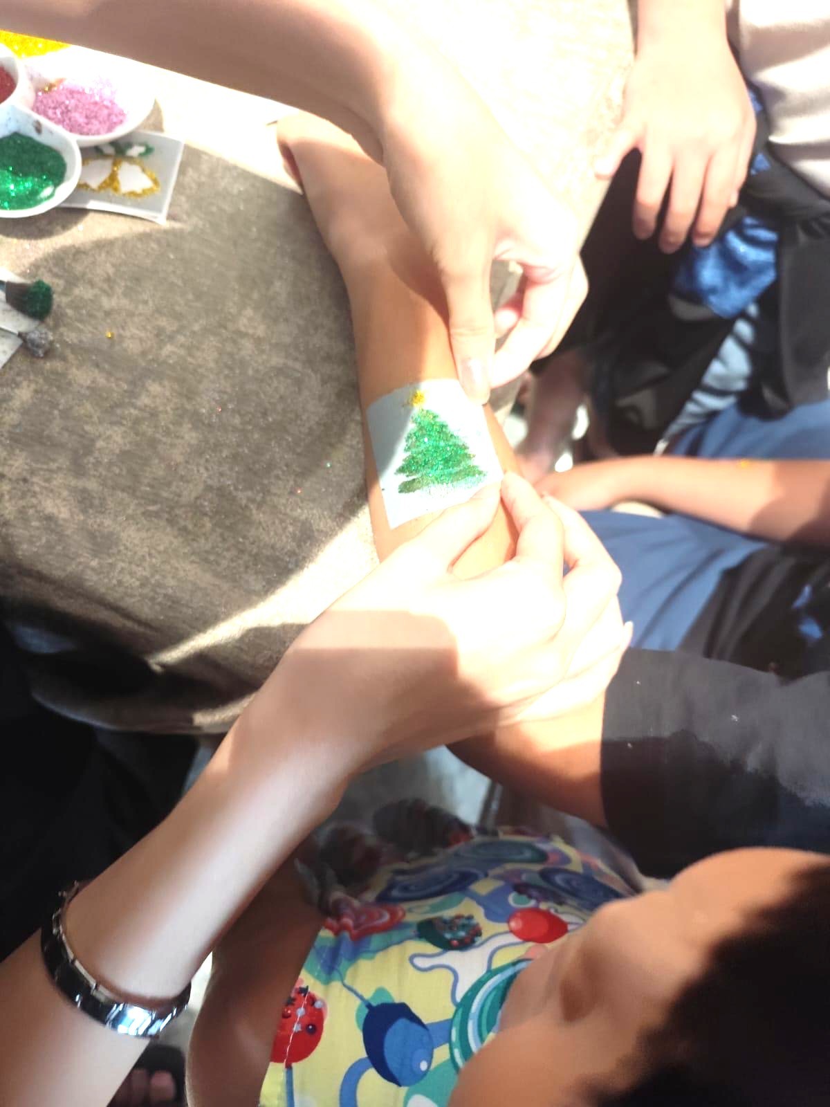 Kids designing glitter tattoo Christmas tree fringe activity in Singapore